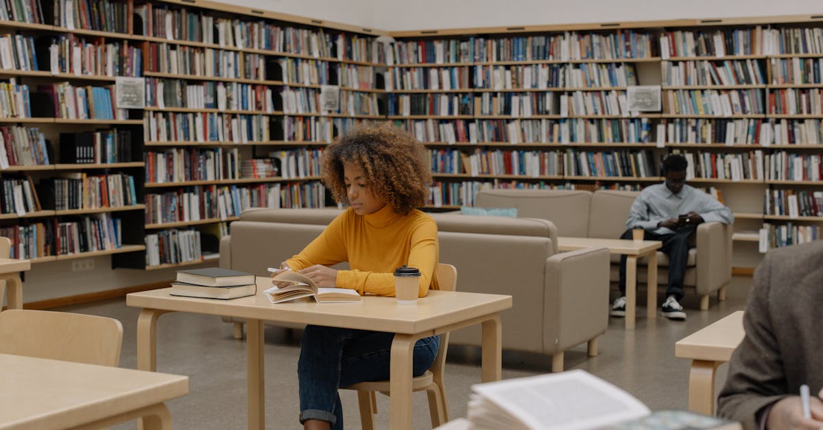 Students studying in a university library surrounded by bookshelves and tables.